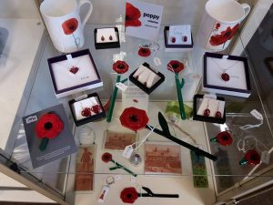 Various items with a poppy theme, mainly made of glass arranged on a display shelf