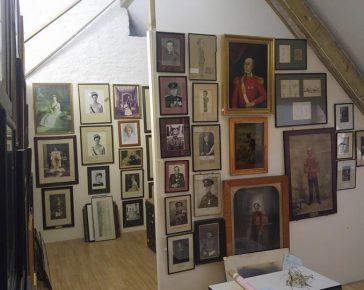 A light attic room with old pictures, portraits and photographs of various sizes, shapes and colours hanging from floor to ceiling