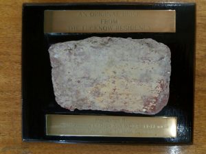 A small and deteriorated brick mounted on a wooden base, with an unreadable brass plaque