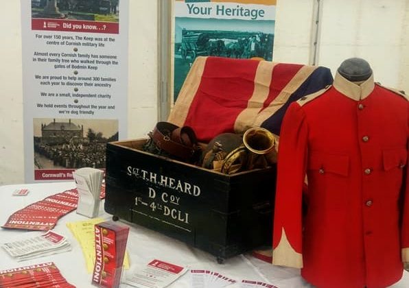 Cornwalls Regimental Museum on the Road! A display of items (including a flag, red military jacket and a bugle) arranged in a wooden chest, surrounded by leaflets, in a white marquee.
