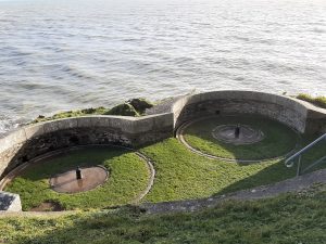 Looking down onto two round structures in the grass on the coast at Fowey, former gun empolacements for coastal defence.