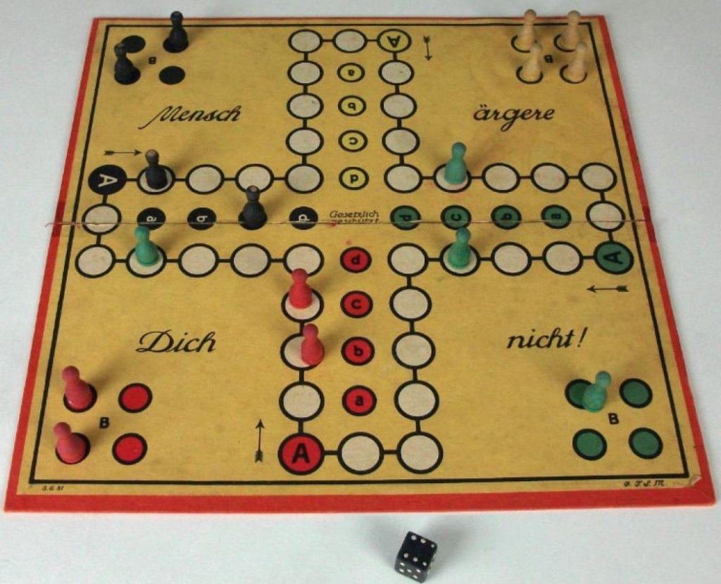 German Board game called ‘Don’t Get Annoyed With Me’. Markers of four different colours are positioned at different points on the board. A six sided black dice lies below the board. 